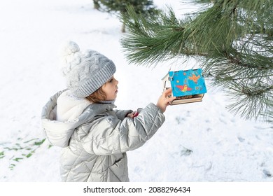 Child Girl Feeding Birds In Winter. Bird Feeder In Snowy Tree, Helping Birds During Cold Season, Teaching Kids To Love And Protect Nature