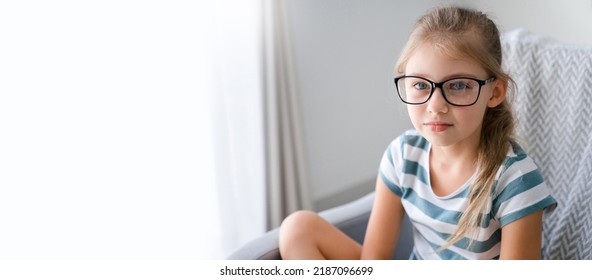 Child Girl In Glasses At Home. Portrait Of Beautiful Blonde Teenager Sitting On Sofa. Charming Female Adolescent Looking At Camera. Mental Health, Solitude In Covid Pandemic And Lockdown. Copy Space