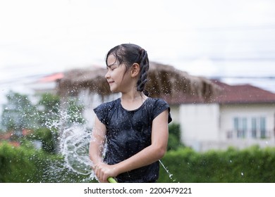 Child Girl Has Fun Playing In Water From Hose Outdoors. Kid Girl Cleaning Mud Dirty By Water From Hose Outside