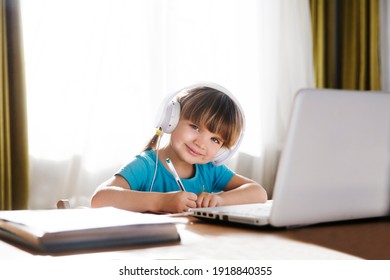 Child Girl In Headphones Is Using A Laptop And Study Online With Video Call Teacher At Home. Homeschooling, Distant Learning