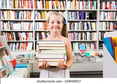 Child Girl Holding A Stack Of Books In The Library