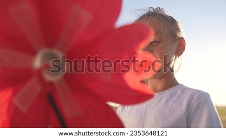 child girl looking at the windmill a toy in the park. happy family childhood lifestyle dream concept. daughter girl playing with a toy windmill in nature. childhood freedom wind concept outdoors