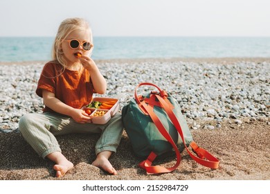 Child girl with lunchbox eating vegetables outdoor travel vacation healthy lifestyle vegan food picnic on beach hungry kid with lunch box snacks and backpack - Shutterstock ID 2152984729
