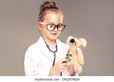 Child Girl In A Medical Gown And Stethoscope Plays And Pretends To Be A Doctor . Children Choose A Profession For The Future. Happy And Smiling Baby In The Game. Expressive Facial Emotions