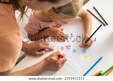 Child girl with mom draw with colored pencils on white paper. Top view, flat lay.