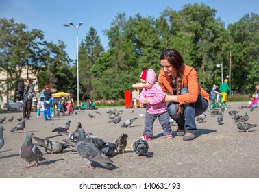 Child Girl And Mum Playing With Doves In The City Street