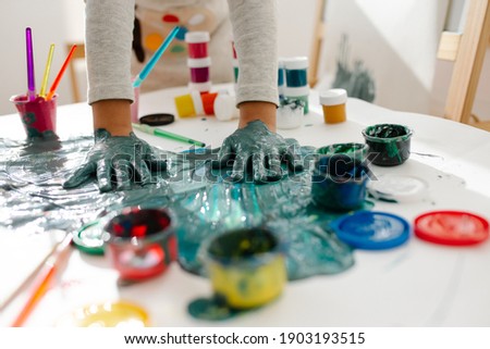 Child girl painting her hand with paint and paintbrush. Finger painting or art therapy for children. Fun activities for toddlers.