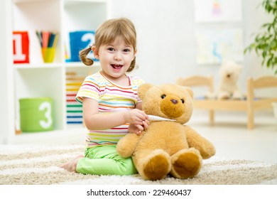 child girl playing doctor with plush toy at nursery