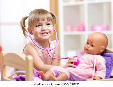child girl playing doctor role game examinating her doll using stethoscope sitting in playroom at home, school or kindergarten