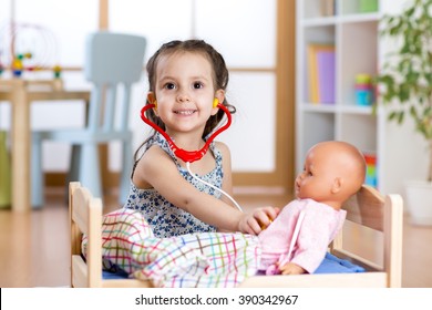child girl playing doctor role game examining her doll using stethoscope sitting in playroom at home, school or kindergarten