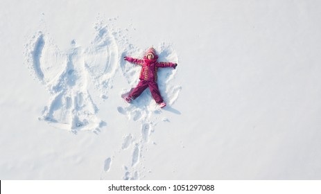 Child Girl Playing And Making A Snow Angel In The Snow. Top Flat Overhead View