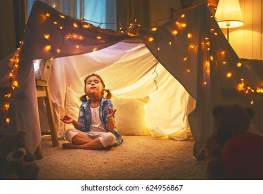 Child Girl Playing Meditates In Yoga Pose In Tent At Home Before Going To Bed
