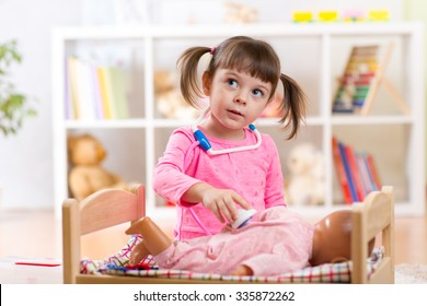 Child girl plays doctor examining baby doll patient with toy stethoscope