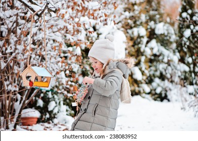 Child Girl Pour Seeds In Bird Feeder In Winter Snowy Garden