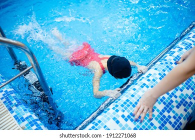 Child Girl Is Practicing Swimming In Pink Bathing Suit In Pool, Coach Will Conduct Training Swim.