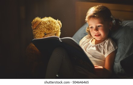 Child Girl Reading A Book In Bed Before Going To Sleep