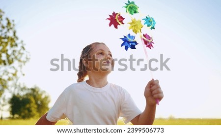 child girl running with windmill a toy in the park. happy family kid dream concept. daughter girl playing with a toy windmill in nature outdoor. childhood freedom wind concept