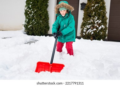 Child Girl Shoveling Fresh Snow And Clearing Sidewalks Near Home. Girl Removaling Snow With Shovel. Little Helper For Parents. Winter Kids Fun Outdoor Activities 