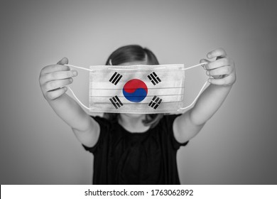 A Child Girl Show A Protective Medical Mask Against Bacteria And Viruses With The Flag Of South Korea.