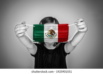 A Child Girl Show A Protective Medical Mask Against Bacteria And Viruses With The Flag Of Mexico.