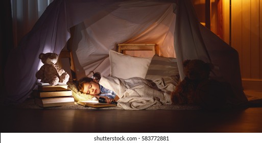 child girl sleeping in a tent with a book and a flashlight home