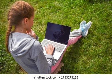 Child Girl Is Studying Remotely. Distance Education. A Kid With A Laptop Outside. Home Schooling