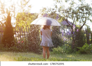 Child Girl With An Umbrella Plays Summer Rain In The Garden. Summer Time.