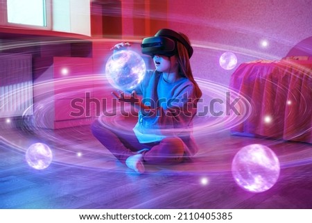 Child girl wearing virtual reality headset and looking at digital space system with planets or Universes. Space exploration with augmented reality glasses. She is sitting on floor at childroom.