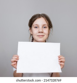 Child Girl In A White T-shirt Holding Awhite Paper,  Mockup.portrait Of A Teenage Girl With Blue Eyes. Selective Focus