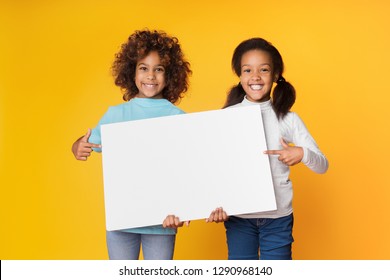 Child girls holding empty banner and pointing on it, copy space, yellow background