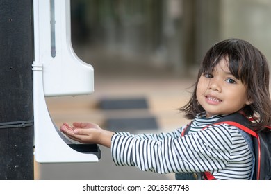 Child girls kid using automatic alcohol gel dispenser spraying on hands sanitizer machine antiseptic disinfectant, new normal life after Coronavirus COVID-19 pandemia.