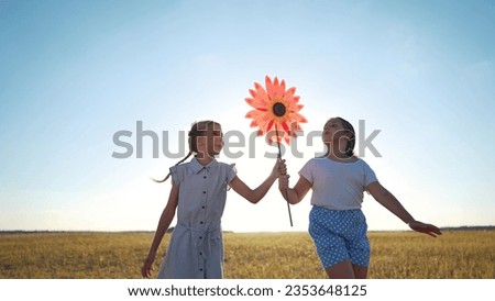 child girls running with windmill a lifestyle toy in the park. happy family kid dream concept. daughters girls playing with toy windmill in nature. childhood freedom wind lifestyle concept outdoors