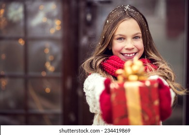 Child Giving A Christmas Present Near Her House Door, Snowy Outside