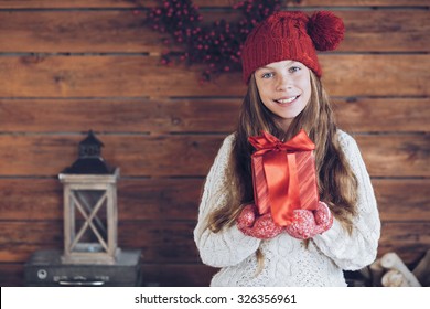 Child Giving A Christmas Present On Rustic Wooden Background, Farmhouse Interior.