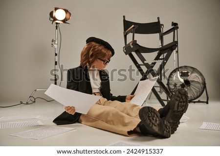 child in glasses and beret reading screenplay and sitting on floor, boy as director of filmmaker