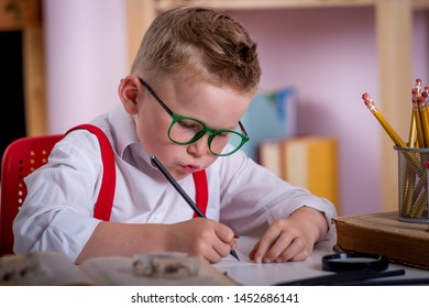 Child In Glasses Learning Math And Numbers In Class. Kid Reading A Book While Sitting On Desk. Pupil Holding Pen And Writing In Notebook. Back To School. Student Doing Test In Primary School.