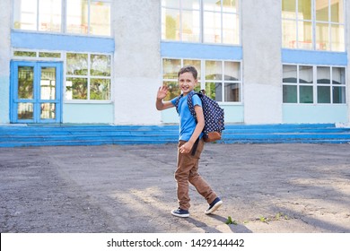 The Child Goes To School. The Boy In The Morning, Goes To School. Portrait Of A Happy Child With A Briefcase On His Back. Concept Student Goes To School And Waving Goodbye. Free Text, Copy Space.