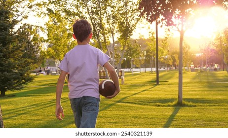 A child going holding in his hand rugby ball in park. a silhouette of a child with a ball in a green park. - Powered by Shutterstock