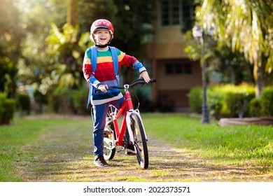 Child Going To School On Bike. Kids Ride Bicycle. Safe Way To Elementary School. Little Boy With Backpack On Red Bike Wearing Safety Helmet. Healthy Outdoor Activity For Young Student.