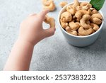 Child grabbing a cashew nut served in a bowl. Group of large roasted cashew nuts