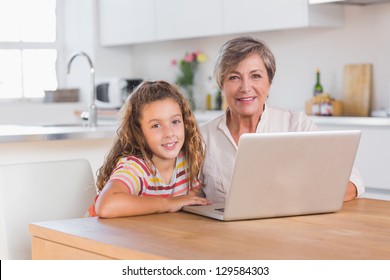 Child and granny looking at the camera with laptop in kitchen - Powered by Shutterstock