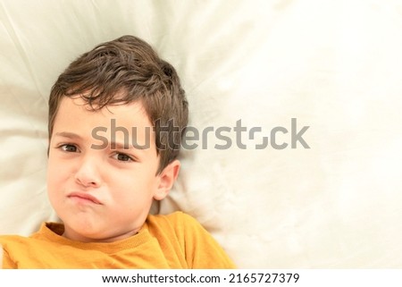 Child grimaces while lying in bed. Funny, dissatisfied kid face, portrait. Sad caucasian brunette boy, 7 years old. Eye contact. Concept of aggression, psychology, relationships, childhood, parenthood Stock photo © 