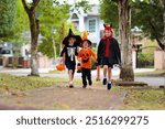 Child in Halloween costume. Kids trick or treat on suburban street. Little boy and girl with pumpkin lantern and candy bucket. Baby in witch hat. Autumn season holiday fun.  Friends play outdoor.