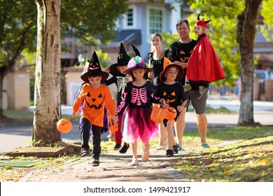 Child in Halloween costume. Mixed race Asian and Caucasian kids and parents trick or treat on street. Little boy and girl with pumpkin lantern and candy bucket. Baby in witch hat. Autumn holiday fun. - Shutterstock ID 1499421917