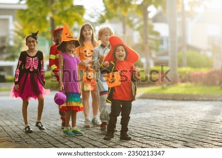 Child in Halloween costume. Mixed race kids and parents trick or treat on street. Little boy and girl with pumpkin lantern and candy bucket. Baby in witch hat. Autumn holiday fun.