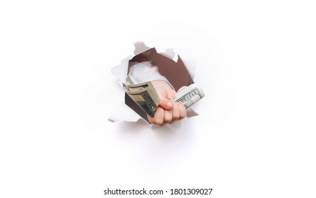 A Child Hand Appears In The Hole In Torn White Paper And Squeezes Two Hundred-dollar Bills. The Concept Of Alimony Poverty, Benefits, Scholarships, And Stinginess. Background With Copy Space.