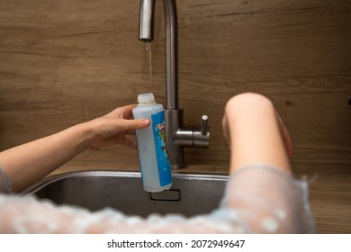 Child Hand Filling The Pet Water Bottle In The Kitchen At The Tap. Selective Depth Of Field, Only One Hand With Water Bottle Sharp, Rest Out Of Focus.