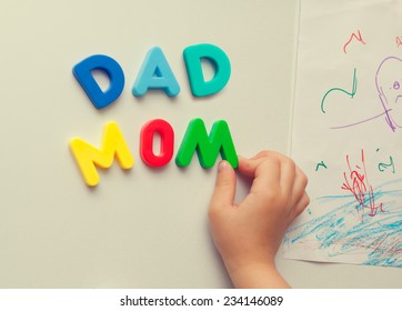 Child Hand Forming Mom And Dad Words With Magnetic Letters On Refrigerator Door.