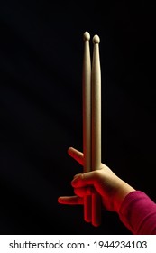 Child Hand Hold Wooden Drum Sticks. Showing Devil Horns Sign, Symbol Of Heavy Metal On Black Backlit Red Background. Rock Music Concept. Unrecognizable. Soft Focus