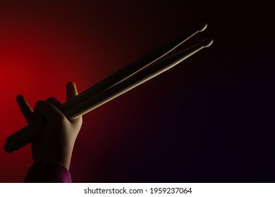 Child Hand Hold Wooden Drum Sticks Showing Devil Horns Sign, Symbol Of Heavy Metal On Background Vivid Backlit. Rock Music Concept. Unrecognizable. Advertising Drum Lessons For Children. Soft Focus